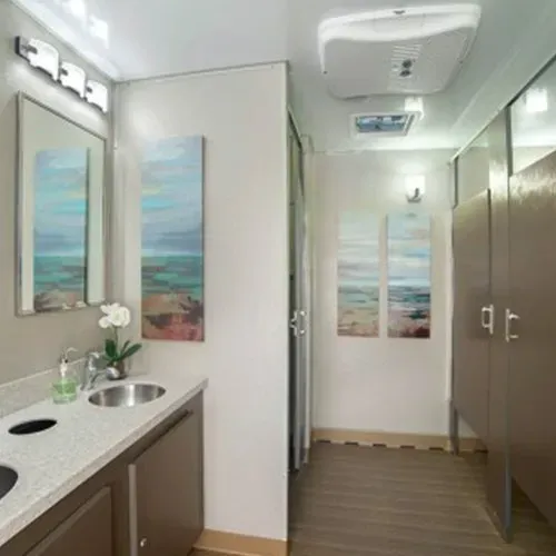 Spacious portable restroom trailer with mirror, sinks, and various stalls.