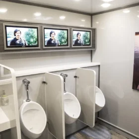 Ultra-luxury portable restroom trailer with TVs, urinals, and modern sink area.