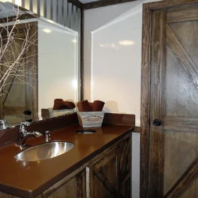 Portable restroom trailer featuring rustic decor, wood accents, and a barn-style door.