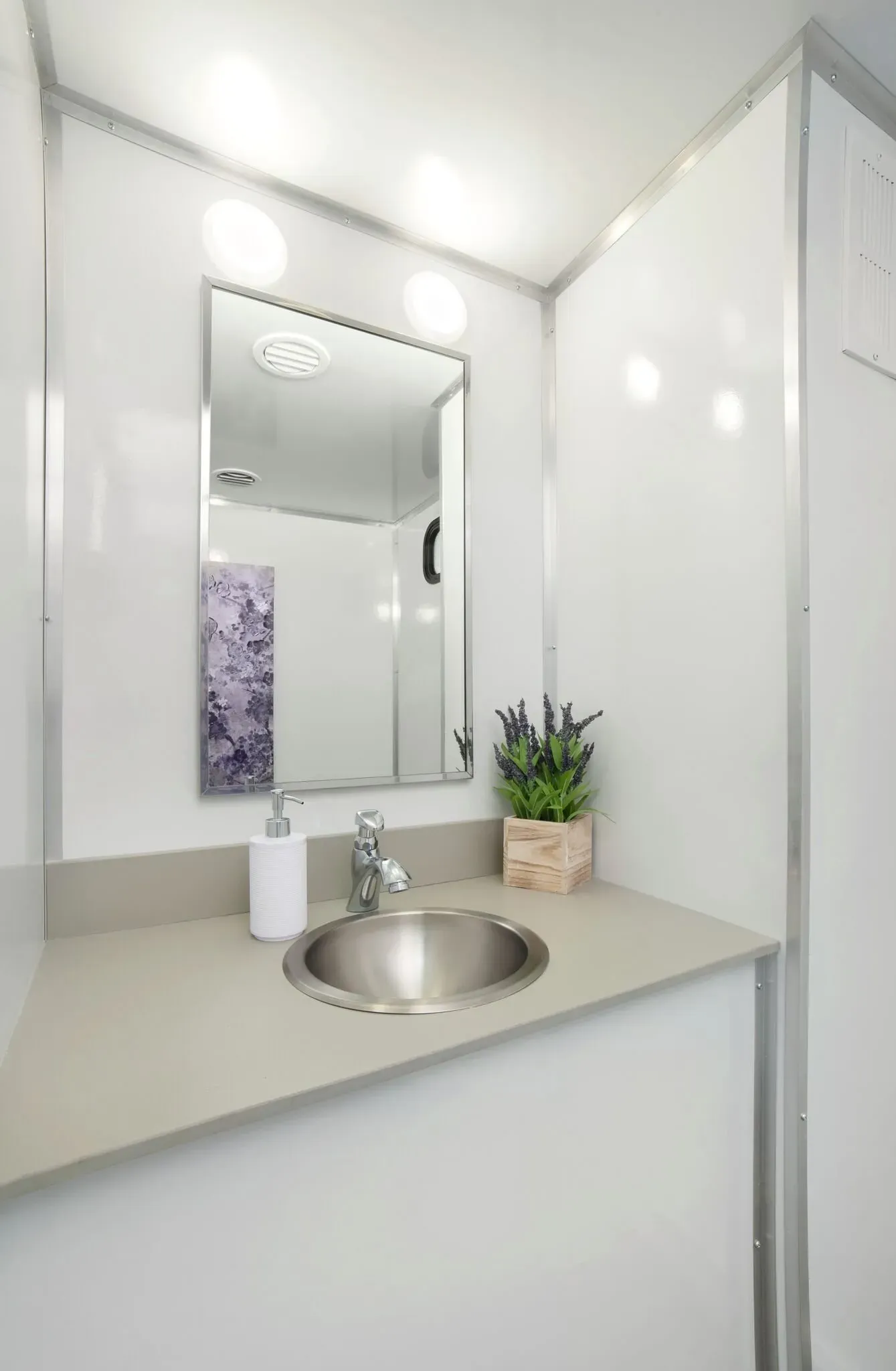 Portable restroom trailer sink area with mirror and soap dispenser.
