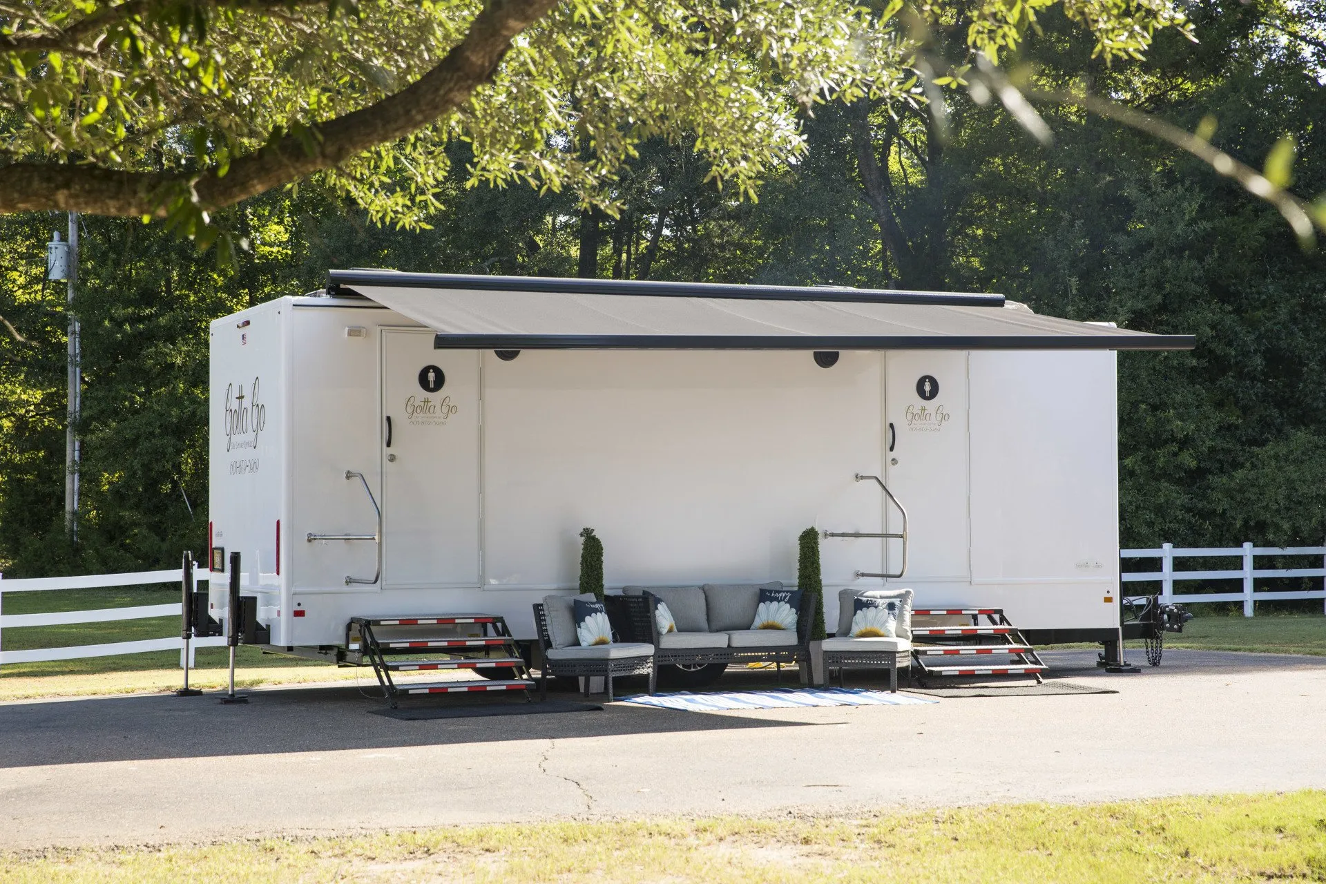 Portable restroom trailer with steps and awning in a park setting.