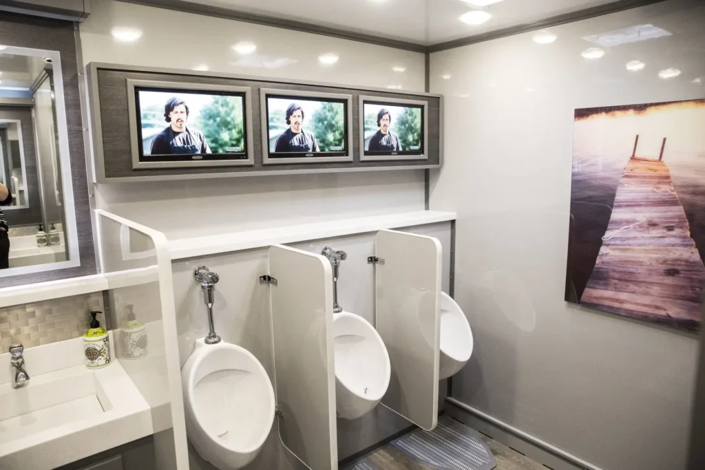 Ultra-luxury portable restroom trailer with TVs, urinals, and modern sink area.