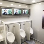 Ultra-luxury portable restroom trailer with TVs, urinals, and modern sink area.